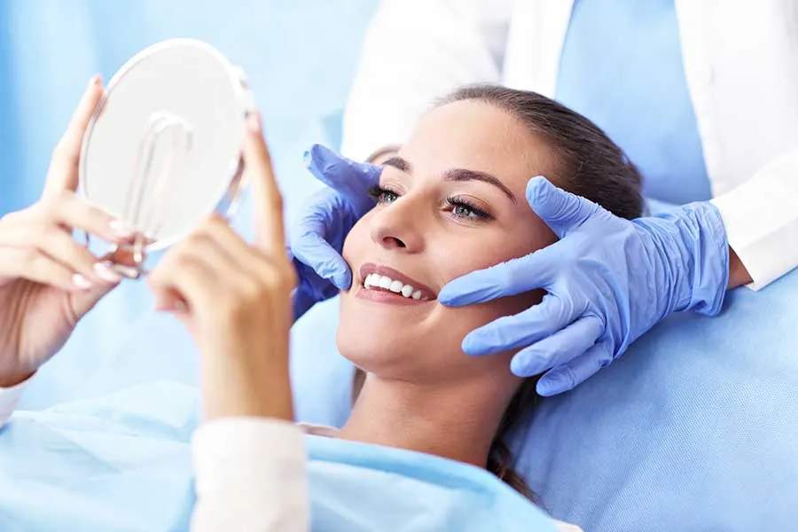 Young woman smiling while looking at a hand-held mirror during her dental examination. 